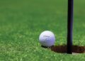 Close-up of a golf ball near a hole on a vibrant golf green, capturing the moment of near success.